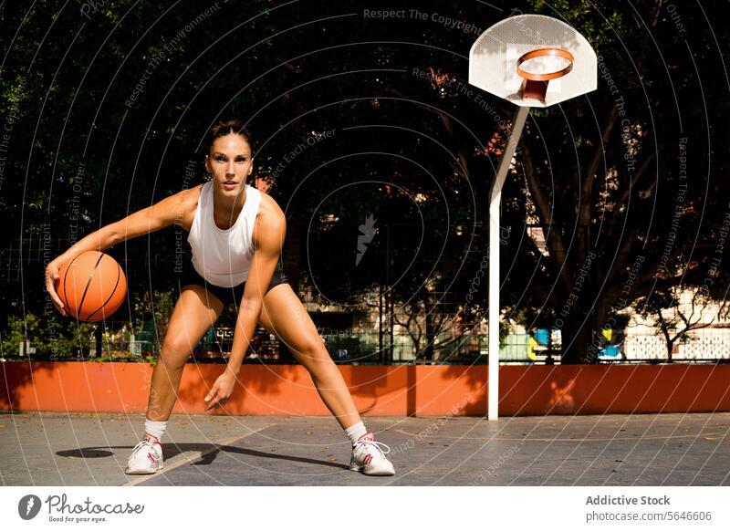 Full body of sporty young female in activewear looking at camera while playing basketball on court during sunny summer day Sportswoman Basketball Play Court