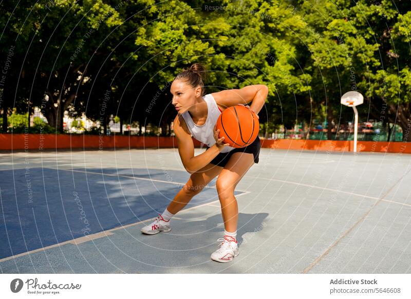 Full body of sporty young female in activewear looking away while playing basketball on court during sunny summer day Sportswoman Basketball Play Court Dribble