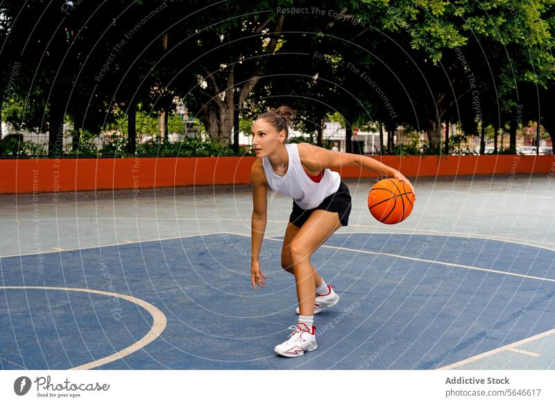 Full body side view of sporty young female in activewear looking away while playing basketball on court during sunny summer day Sportswoman Basketball Play
