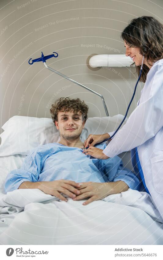 Physician examining patient lying on bed with stethoscope in clinic man doctor smile happy nurse check up examine hospital uniform health care diagnostic
