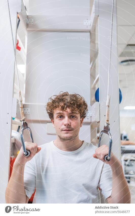 Young man standing in hospital and holding hanging holders patient calm clinic curly hair interior illness equipment comfort male young health care confident