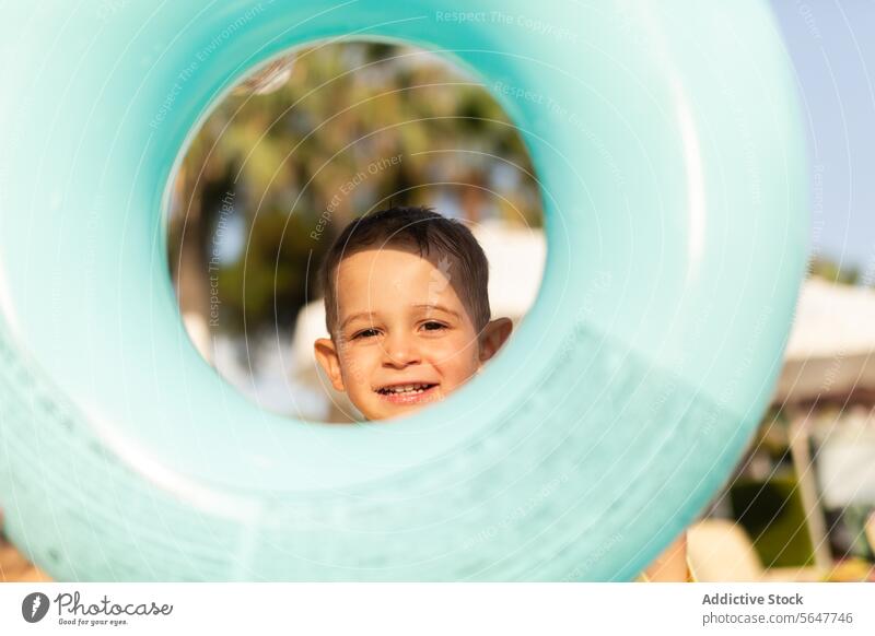 Boy playing peekaboo with swimming ring at the beach boy child float sunny fun outdoor activity playtime summer vacation holiday joy happy smile childhood blue
