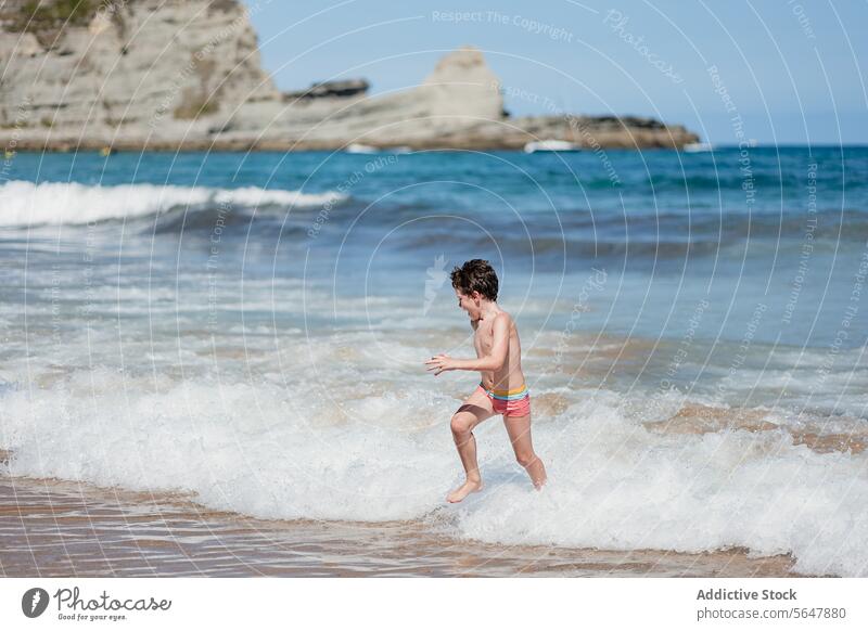 Young boy enjoys playful run on sunny beach wave shore sand sea ocean summer fun child outdoor coast scenic nature vacation holiday travel leisure activity