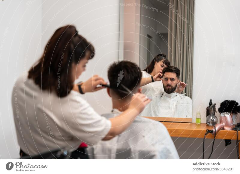 Back view of focused female hairstylist cutting male client's hair with scissors at salon Hairdresser Scissors Cut Comb Man Salon Care Service Haircut Client
