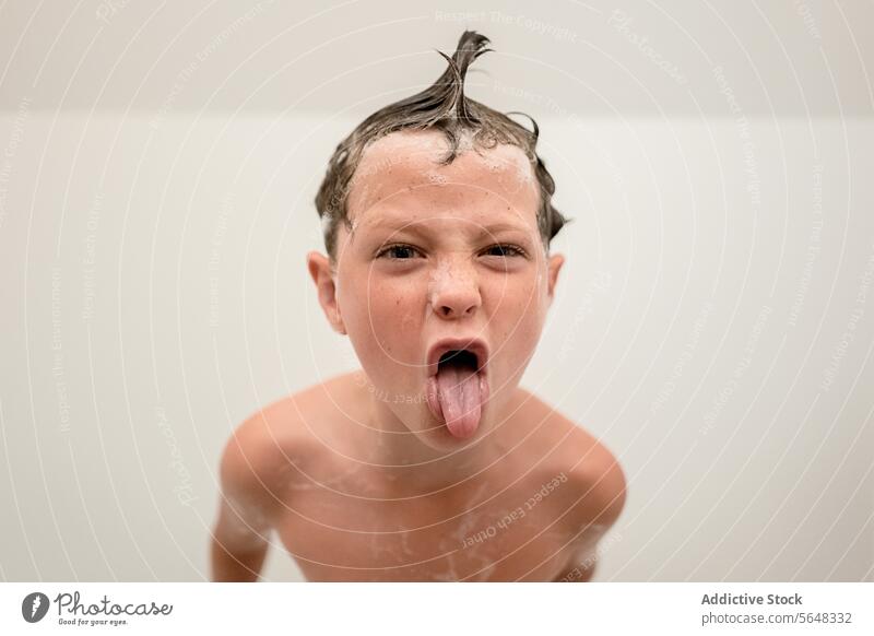 Funny little boy showing tongue out in bathroom foam mouth opened shower hygiene show tongue shampoo wash childhood wet hair kid skin care clean having fun