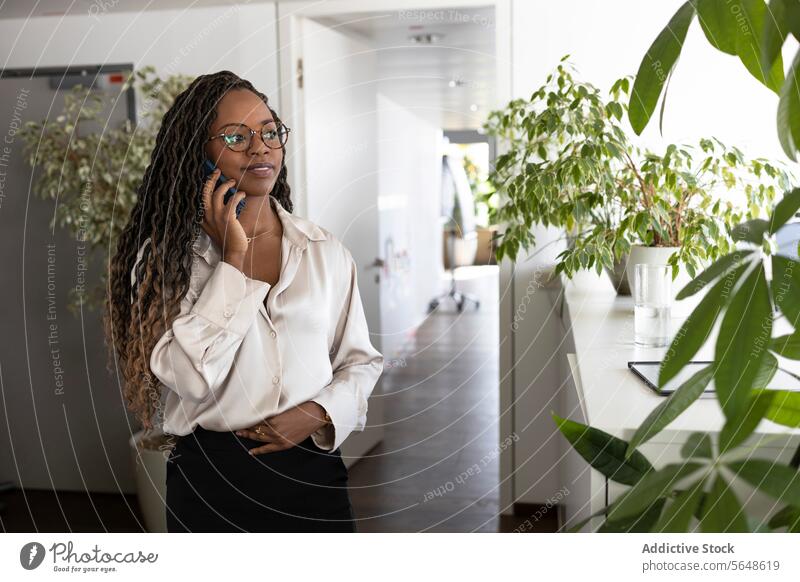 Thoughtful black businesswoman using smartphone in office Businesswoman Smartphone Using Office Smile Happy Hand On Stomach Afro Young Workplace Manager Plant