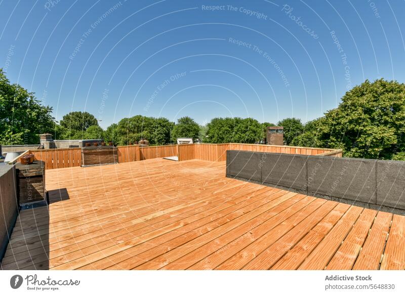 Wooden terrace with trees against blue sky wooden empty neighborhood brown sunny railing floorboard suburb district sunlight property house building modern