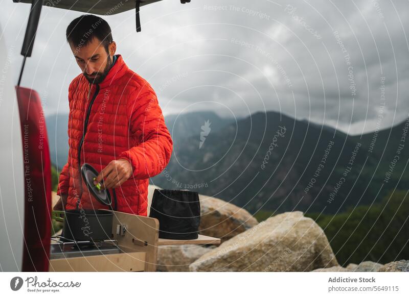 Man in winter jacker cooking food during hiking in countryside Hiker Cook Food Stove Container Mountain Nature Prepare Adventure National Park Winter Jacket