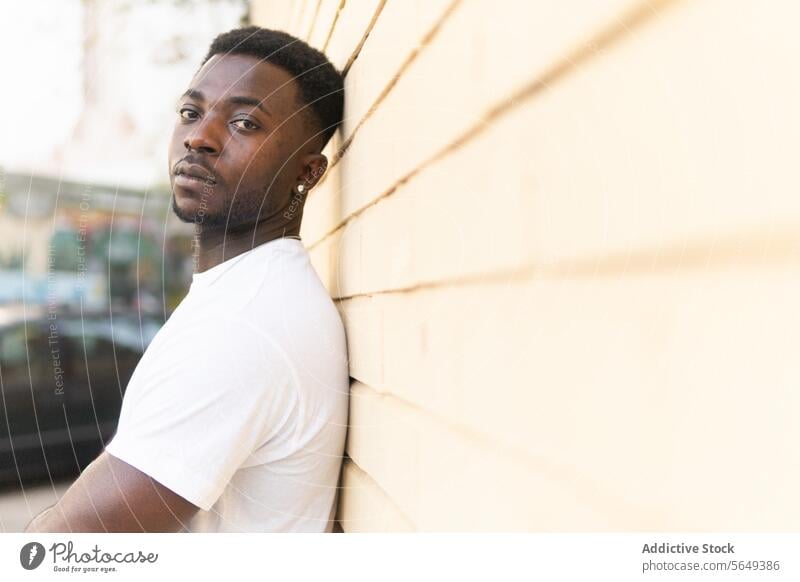 Black man leaning on wall of building lean on brick wall city street portrait urban daytime town emotionless unemotional afro male young african american black