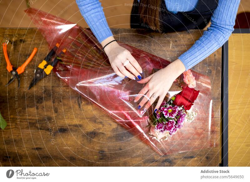 Unrecognizable woman arranging bouquet on table florist plastic wrap flower arrange prepare decoration female young floristry sleeve long hair nail polish