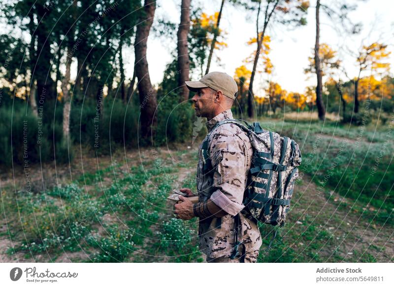 Side view of Army commando with cap and backpack holding box standing in forest soldier military camouflage uniform blurred background army special force