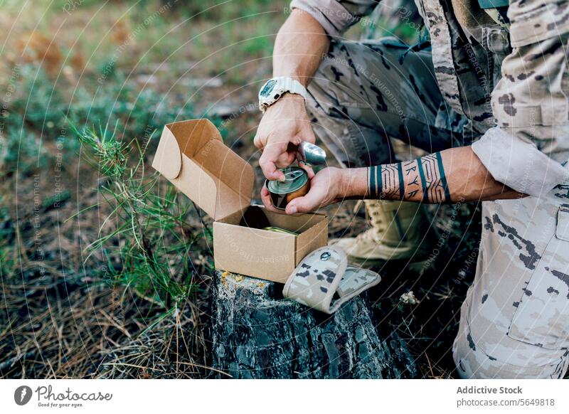 Anonymous Military soldier with backpack opening food can kneeling by box on tree man commando cutlery camouflage forest uniform force blurred background army