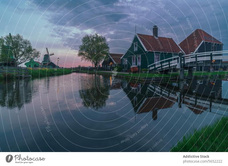A tranquil evening scene with typical Dutch houses and a windmill reflected in the calm waters of Zaanse Schans reflection Netherlands landscape heritage