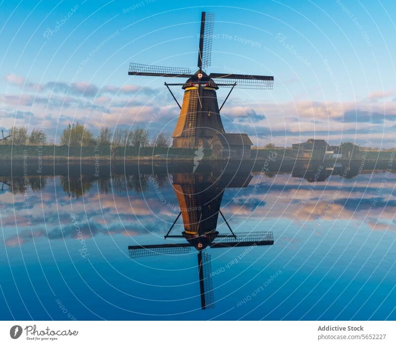 Solitary windmill reflected in the still waters of a Dutch canal at dawn, with a clear blue sky reflection Netherlands serene tranquil traditional culture