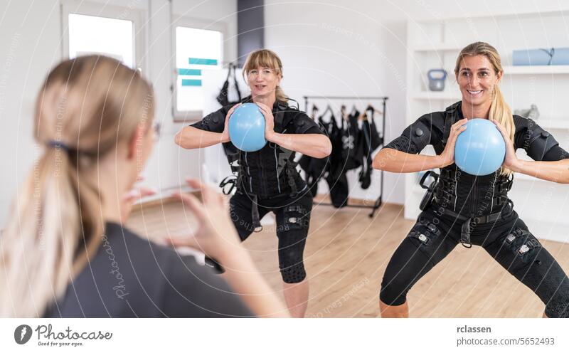 Women exercising with blue gym balls in front of a trainer in a training session and wearing EMS training suits at a EMS Studio. a Royalty Free Stock Photo from Photocase