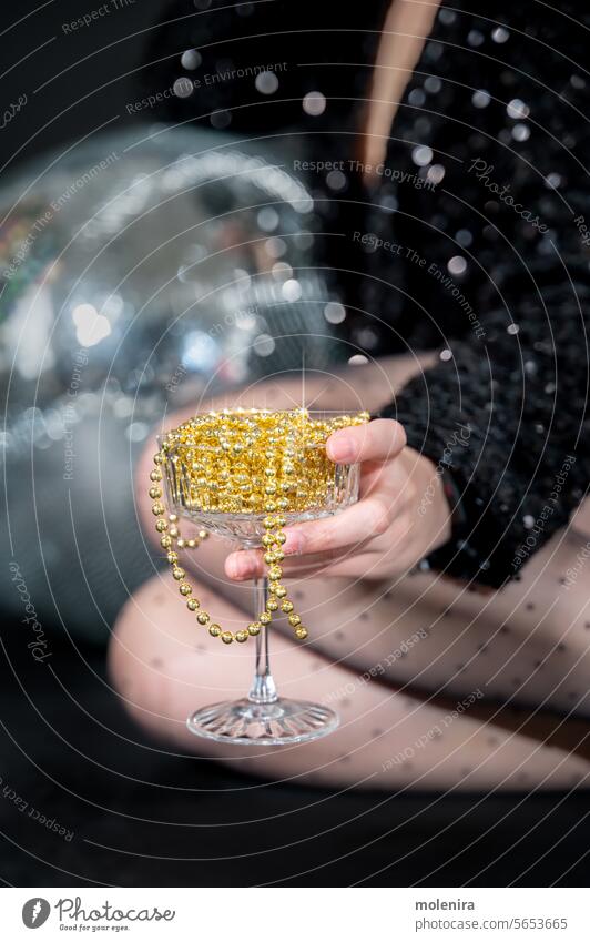 Champagne glass full of Christmas beads as Non-alcoholic drink champagne nonalcoholic mocktail party celebration hand person shimmering disco ball bubbly yellow