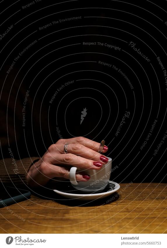 A woman's hand reaching out of the darkness to hold a cup of coffee black coffee cup female finger fingernails fingers nail polish rings spotlight Hand Coffee