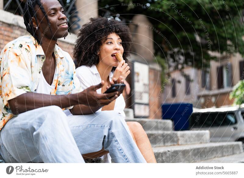 A man and woman sit on steps with the woman eating ice cream and the man holding a phone enjoying Rome atmosphere Man Italy casual clothing floral shirt