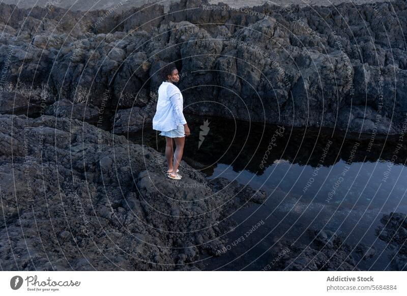 Black woman traveler standing on rocky cliff lake landscape mountain water reflection nature female young african american ethnic black curly hair casual