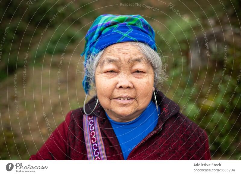 Positive senior woman looking at camera in blurred background in Vietnam stand warm clothes scarf cheerful positive smile countryside winter nature happy aged