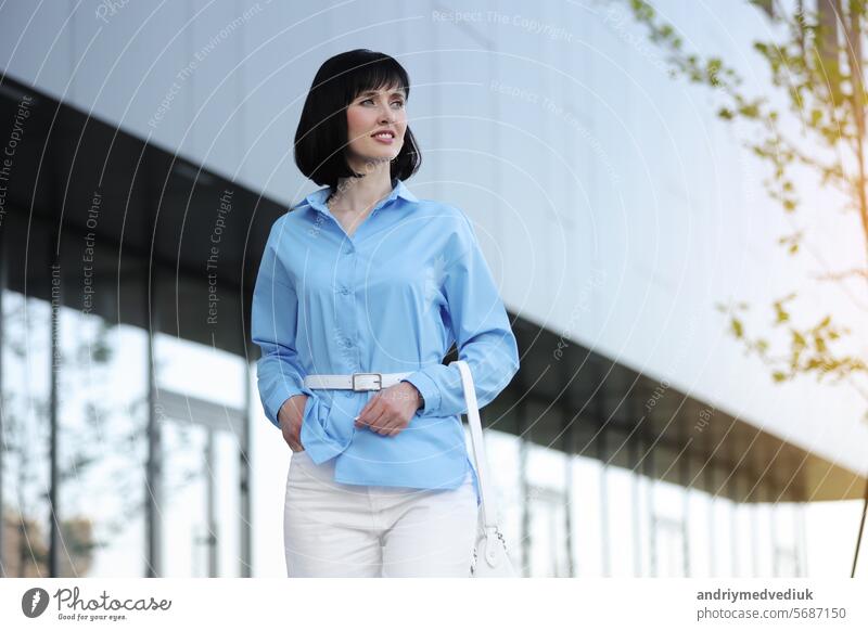 Relaxing and confident young business woman or entrepreneur walks by the modern office building company outdoors. Successful female career. Business people lifestyle, copy space.