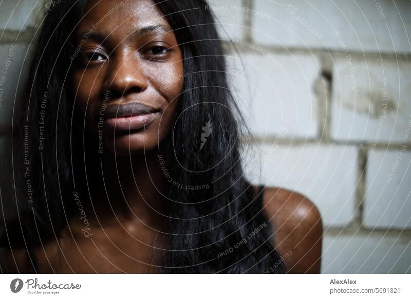 Young, long-haired, slim woman stands in front of a wall of white bricks and into the camera Woman Young woman Long-haired Dark Feminine Human being