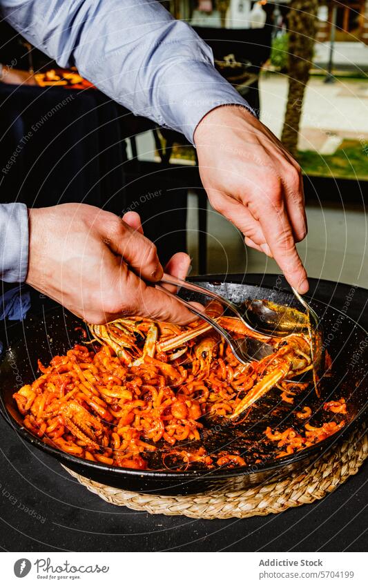 Serving seafood pasta at an outdoor event person serving al fresco dining pan large sumptuous dish meal cuisine cook hand tong culinary gourmet italian sauce