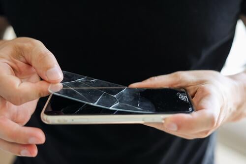 Process unrecognisable repairman is removing broken and old tempered glass screen protector from smartphone, close up view. Services for gluing and replacement of damaged protective glass.