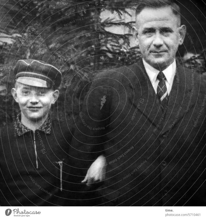 Nephew and uncle in front of fir tree Boy (child) portrait Hand Looking into the camera Dark-haired eyes Man Cap Suit Tie Fir tree Family masculine