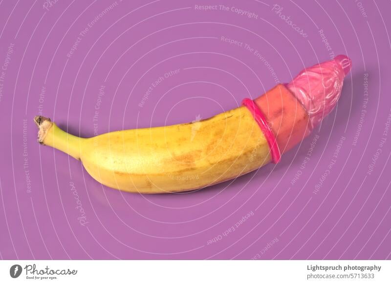 Red condom on banana with purple background. Safe sex concept. symbol sex education sexual issues aids contraceptive erection sex and reproduction protection