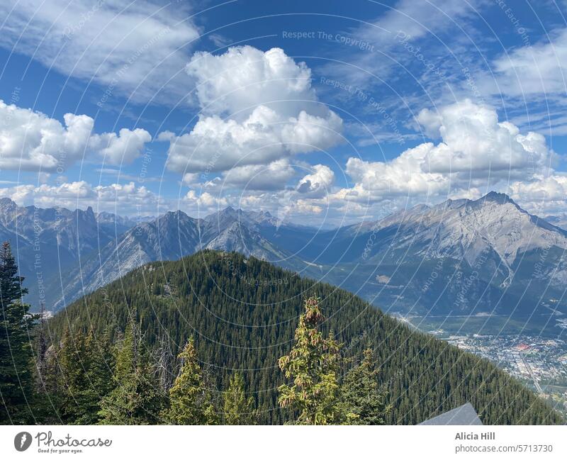 Tree covered mountains in the foreground and snowy mountain in the background. Bright blue skies and fluffy white clouds Mountain nature banff springs