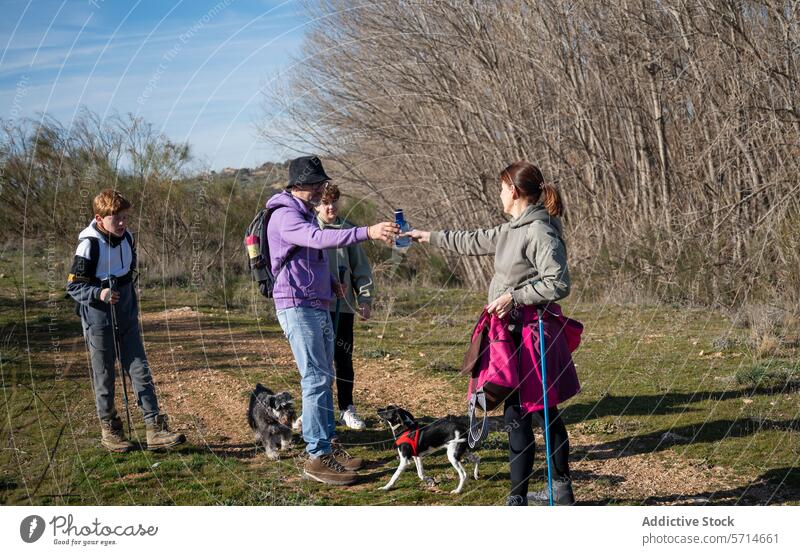 Family members with two dogs on a hike sharing a water bottle, with a young onlooker holding a trekking pole family outdoor activity nature trail hydration