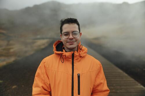 Man in Orange Jacket Enjoying Misty Iceland Landscape iceland travel adventure man male outdoor mist landscape orange jacket smile glasses fog boardwalk nature