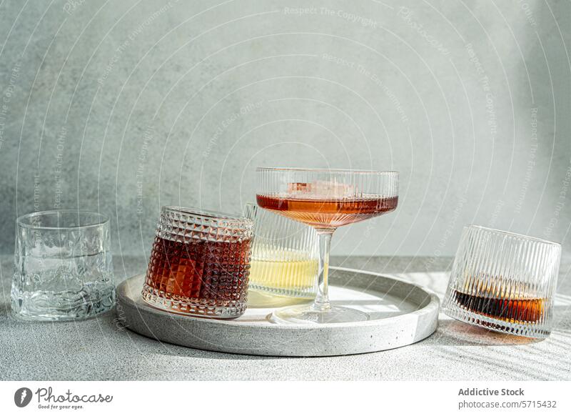 A selection of alcoholic drinks in textured glasses, elegantly displayed on a circular concrete tray with a soft grey backdrop cocktail beverage bar serve