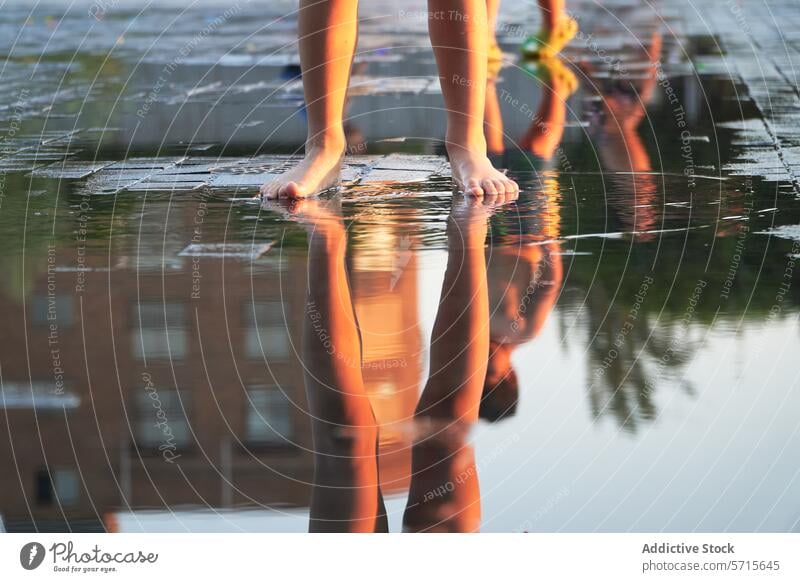 Close-up of anonymous child's feet standing by a reflective puddle, mirroring the warm glow of a city at sunset after rainfall reflection urban water close-up