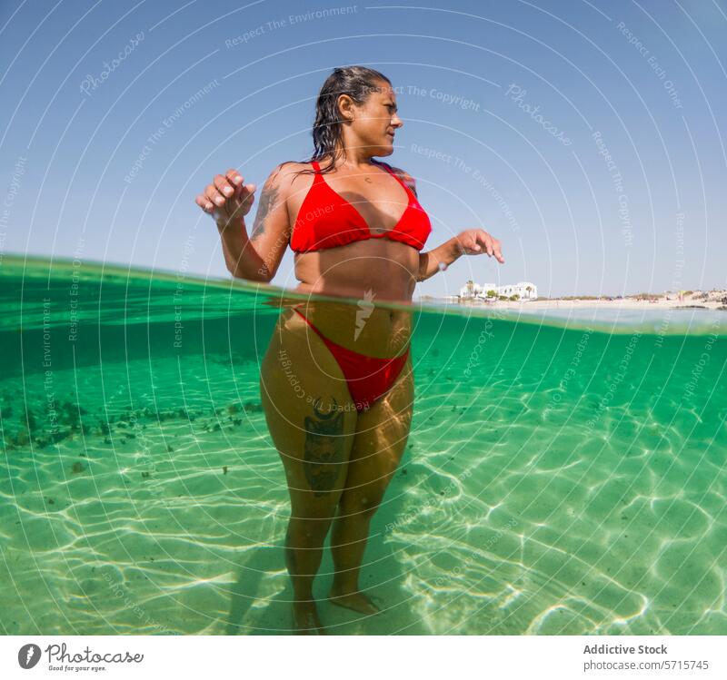 Woman in red swimsuit at clear beach water woman sunny day over-under underwater shot crystal serene environment wading sea ocean shoreline coastline summer