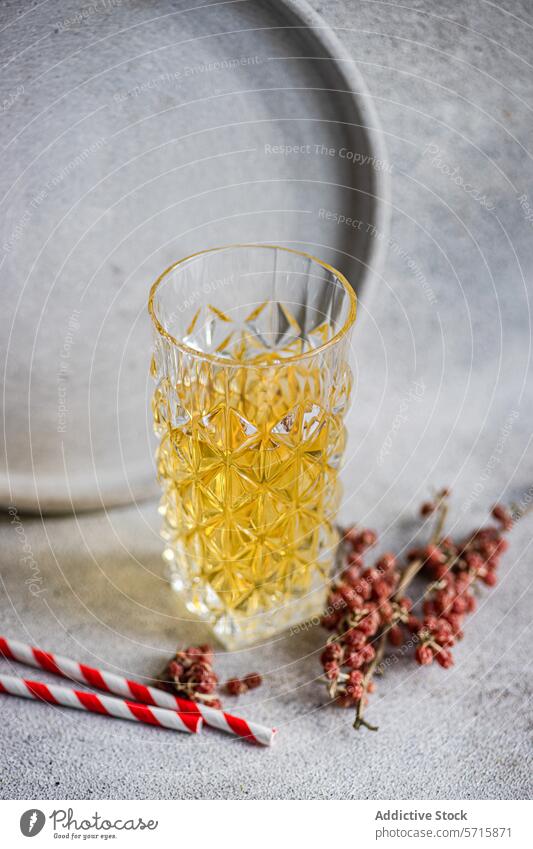 Elegantly textured glass filled with cider beside red berries and a striped straw on a concrete backdrop drink beverage alcohol refreshment elegant crystal