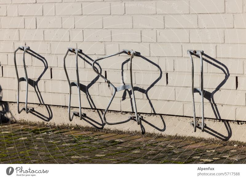 four stands Bicycle rack switch off Bicycle lot Deserted Metal warped bent Broken Parking Colour photo Shadow Shadow play Parking area Parking lot Eco-friendly