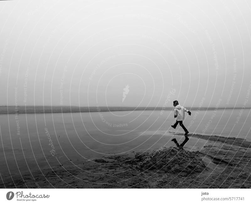 Child runs into the sea on the beach on a foggy day Autumn Autumnal autumn atmosphere Gray somber Dreary Bad weather Lines and shapes Exterior shot