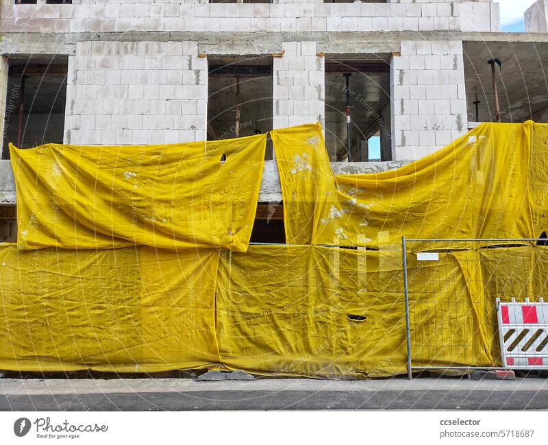 Yellow tarpaulins hanging in front of a building shell unfinished Construction site Architecture Building Manmade structures Work and employment Change