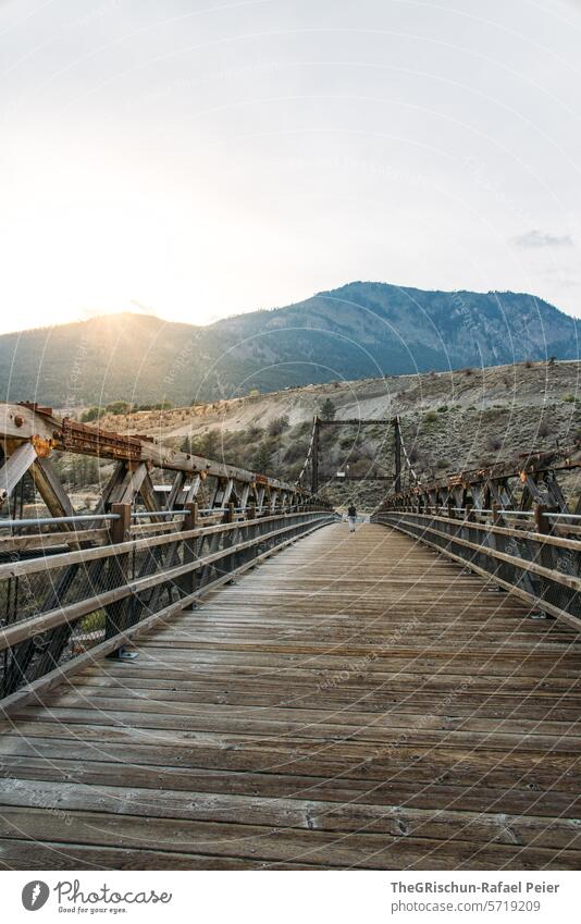 Woman walks over old bridge Wooden bridge Old Bridge Exterior shot Nature Day Back-light Mountain Sunset last sunbeams Walking rail Car bridge Colour photo