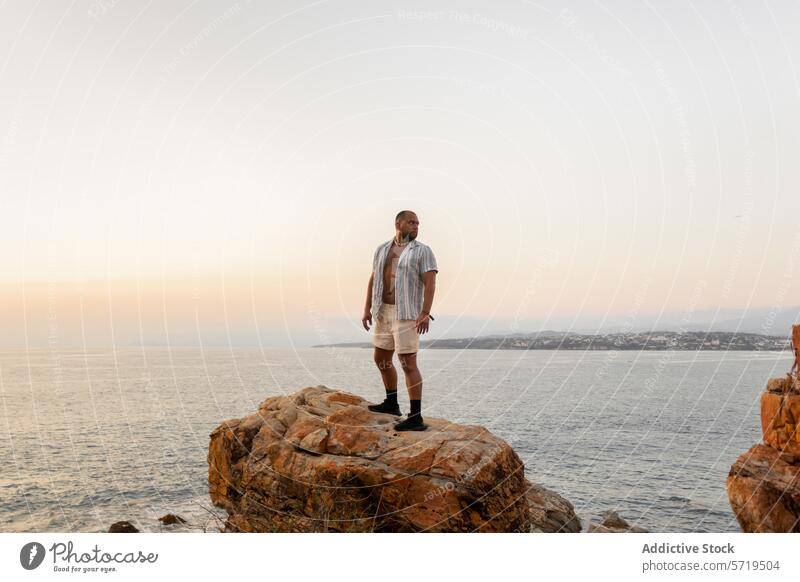 A man stands thoughtfully on a rocky cliff, overlooking the vast ocean as the evening sky softly fades to twilight dusk contemplation coast sea sunset calm