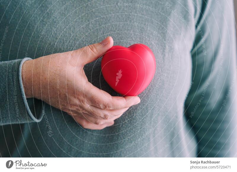 A woman holds a red heart in front of her upper body Woman Heart Heart-shaped Red breast cancer Symbols and metaphors Healthy Foresight Love Emotions Sign