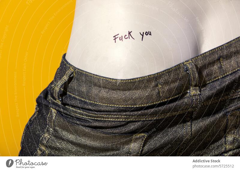 Closeup of a tattoo with the word fuck you denim jeans pocket yellow background symbol casual textile fabric style clothing garment design concept trend