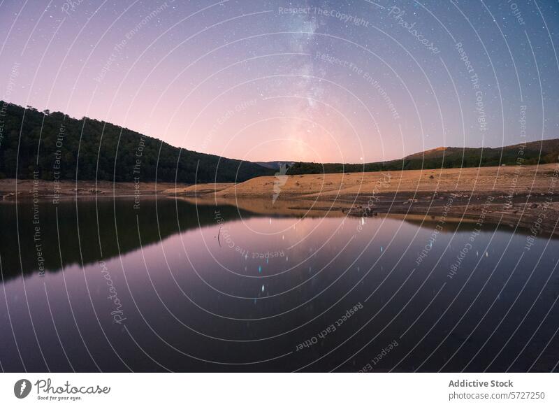 A serene lake reflects a stunning starry night sky with the Milky Way, surrounded by a rugged landscape with visible mudcracks, evoking a sense of peace and isolation