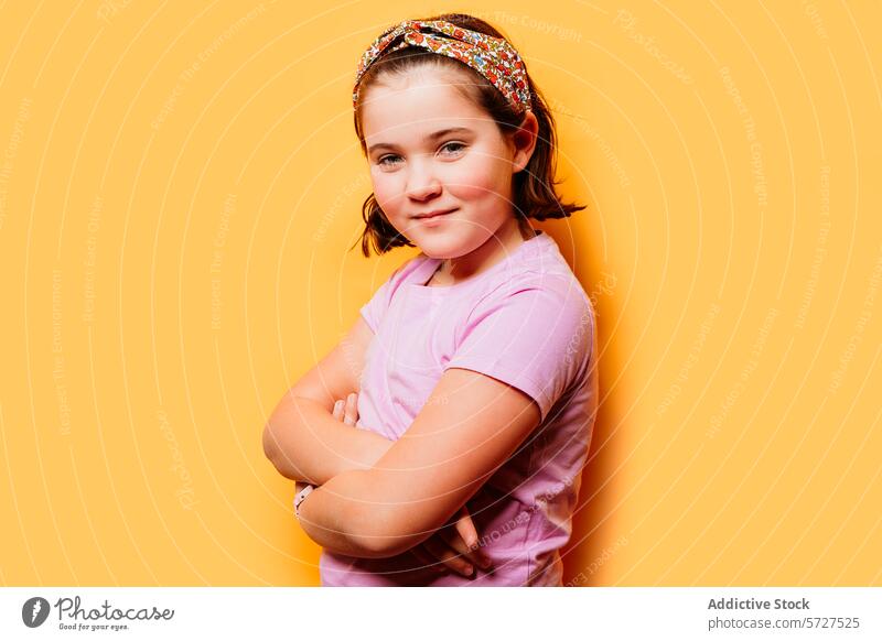 Confident young girl posing with arms crossed on a yellow background child kid confident pose t-shirt headband casual vibrant colorful fashion style cheerful