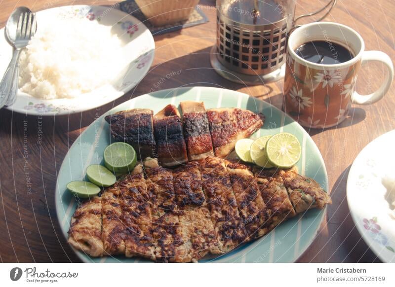 Morning breakfast spread of grilled fish, rice, and coffee in a garden setting, with a French press on a wooden table under the summer sunlight morning french