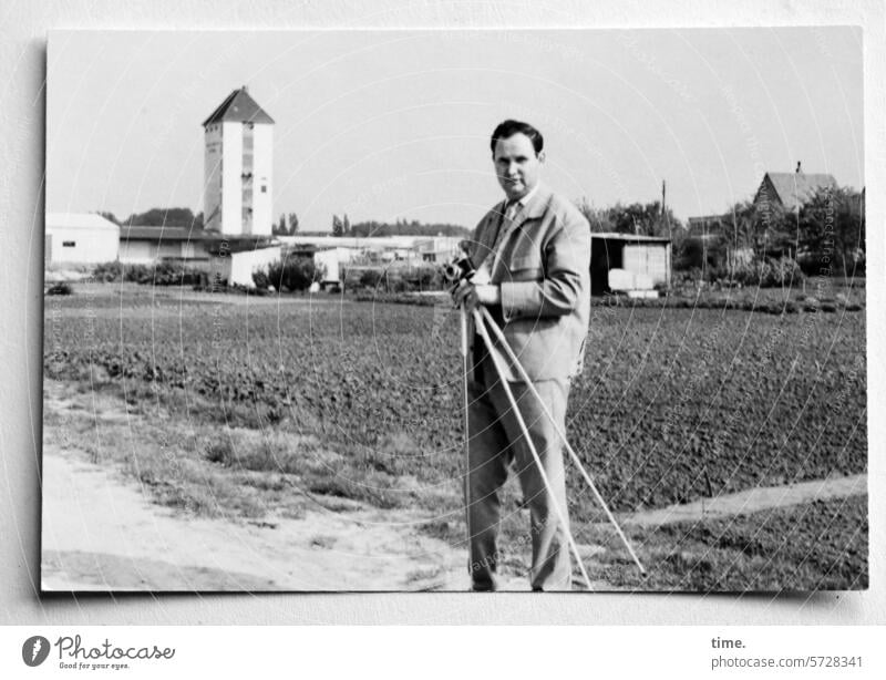 Man with tripod and camera on a dirt road Tripod Landscape Field acre Horizon Outskirts Tower Architecture Jacket Looking into the camera portrait