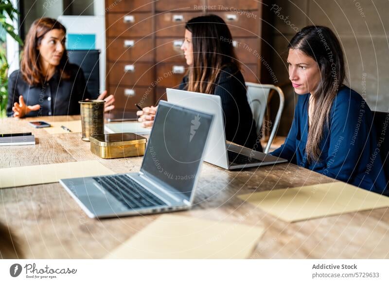 Female professionals in a collaborative meeting at work woman women female colleague discussion wooden table laptop teamwork company women-led business office