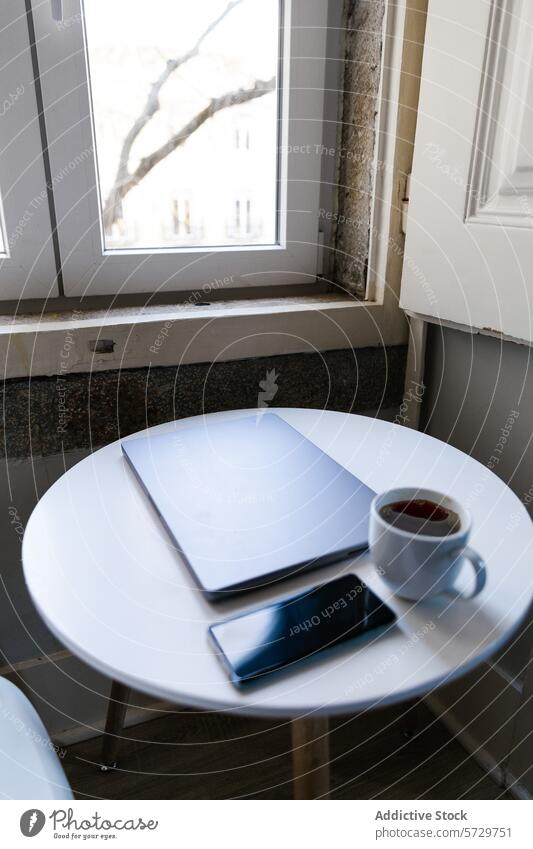 Cozy home office setting with coffee and technology laptop smartphone table window tree tranquility work white table cozy minimalist interior cup beverage drink